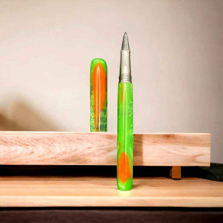 Two pens with green and orange accents on a wooden surface. Made with Alumilite Clear casting resin for woodturning