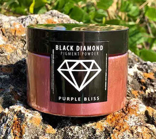 Black Diamond Pigment Powder container labeled 'Purple Bliss' on a rocky surface with greenery.