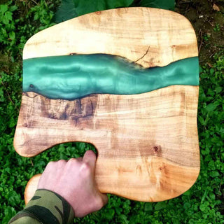 Wooden cutting board with a green resin design held by a hand on grass. Alumilite Amazing Deep Pour Epoxy Resin
